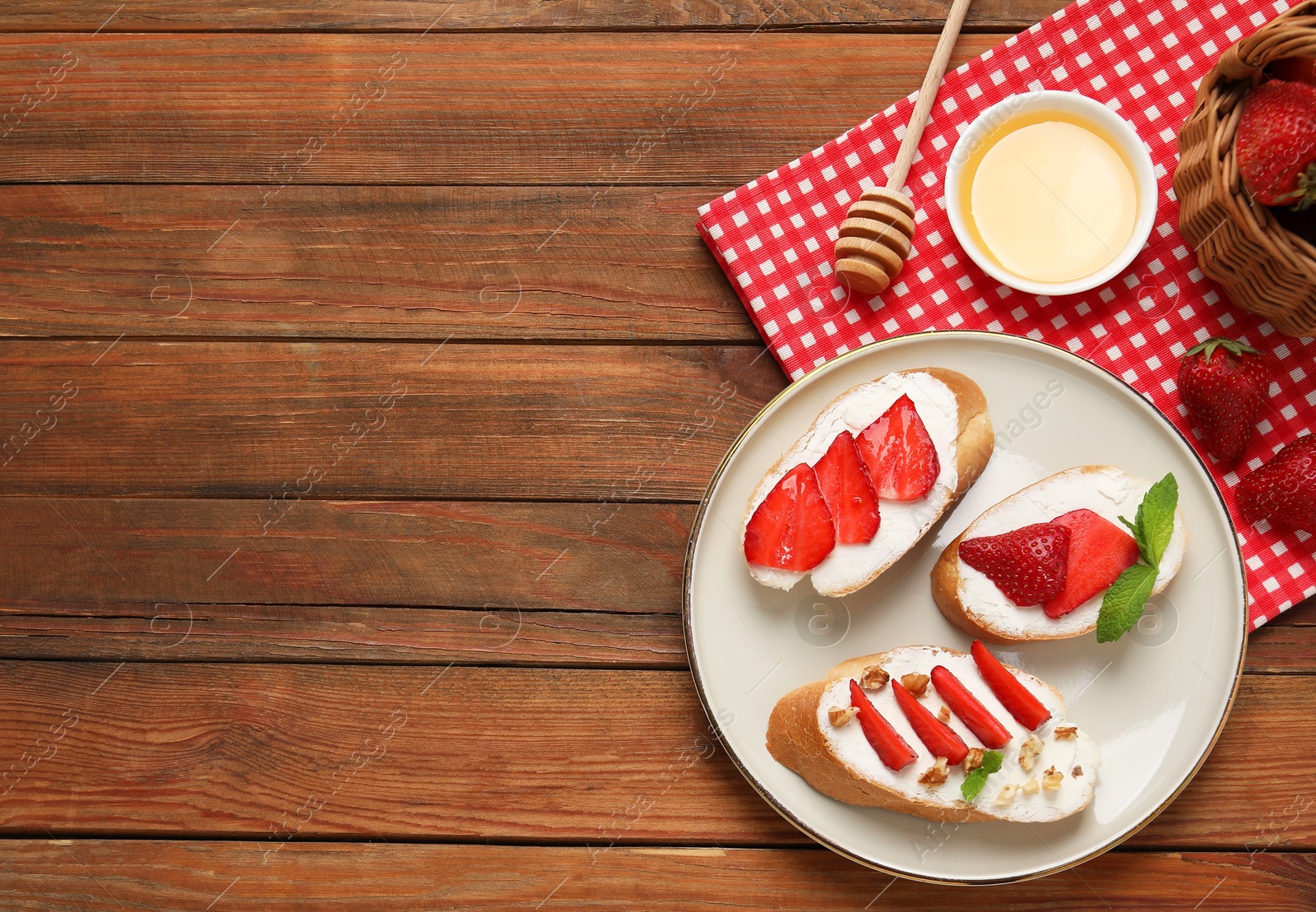 Photo of Delicious bruschettas with ricotta cheese, walnuts, mint, strawberries and honey on wooden table, flat lay. Space for text