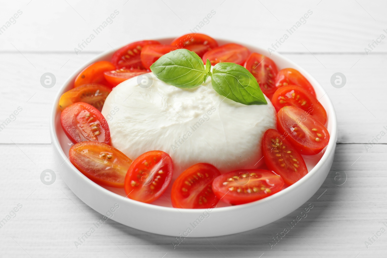 Photo of Delicious burrata cheese, tomatoes and basil on white wooden table, closeup