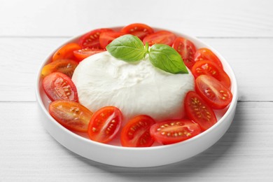 Photo of Delicious burrata cheese, tomatoes and basil on white wooden table, closeup