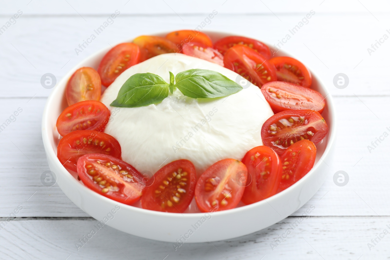 Photo of Delicious burrata cheese, tomatoes and basil on white wooden table, closeup