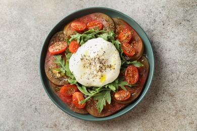 Photo of Delicious fresh burrata salad in bowl on gray textured table, top view