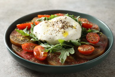 Photo of Delicious fresh burrata salad in bowl on gray textured table, closeup