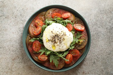 Delicious fresh burrata salad in bowl on gray textured table, top view