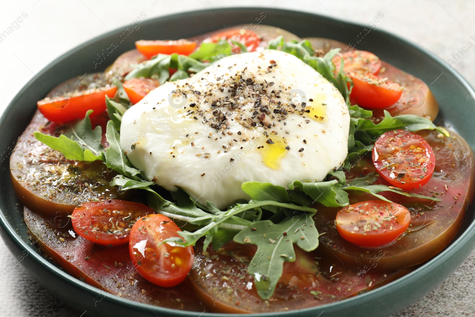 Photo of Delicious fresh burrata salad in bowl on gray table, closeup