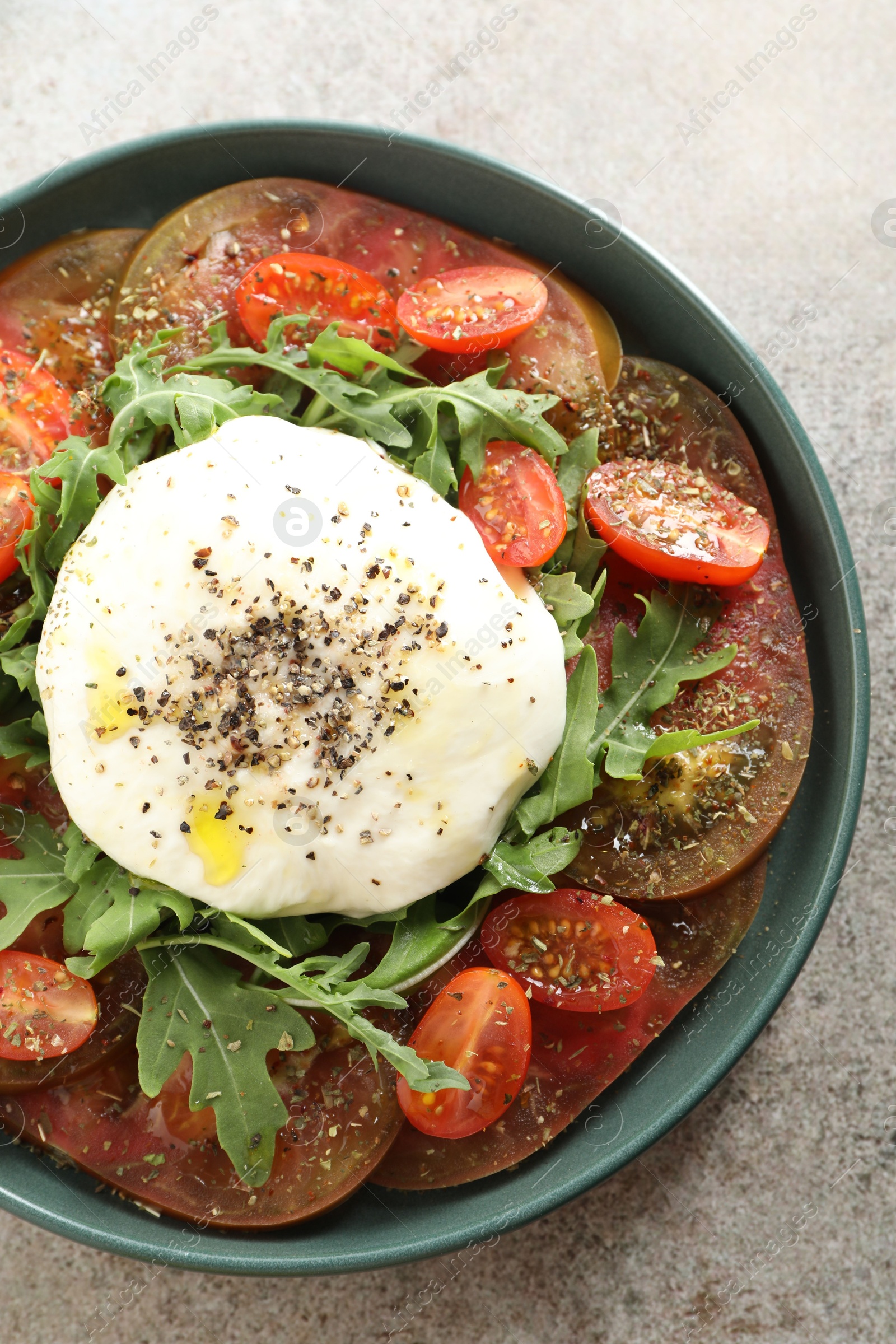 Photo of Delicious fresh burrata salad in bowl on gray textured table, top view