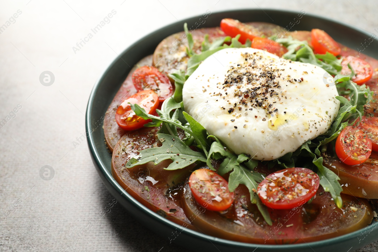 Photo of Delicious fresh burrata salad in bowl on gray textured table, closeup