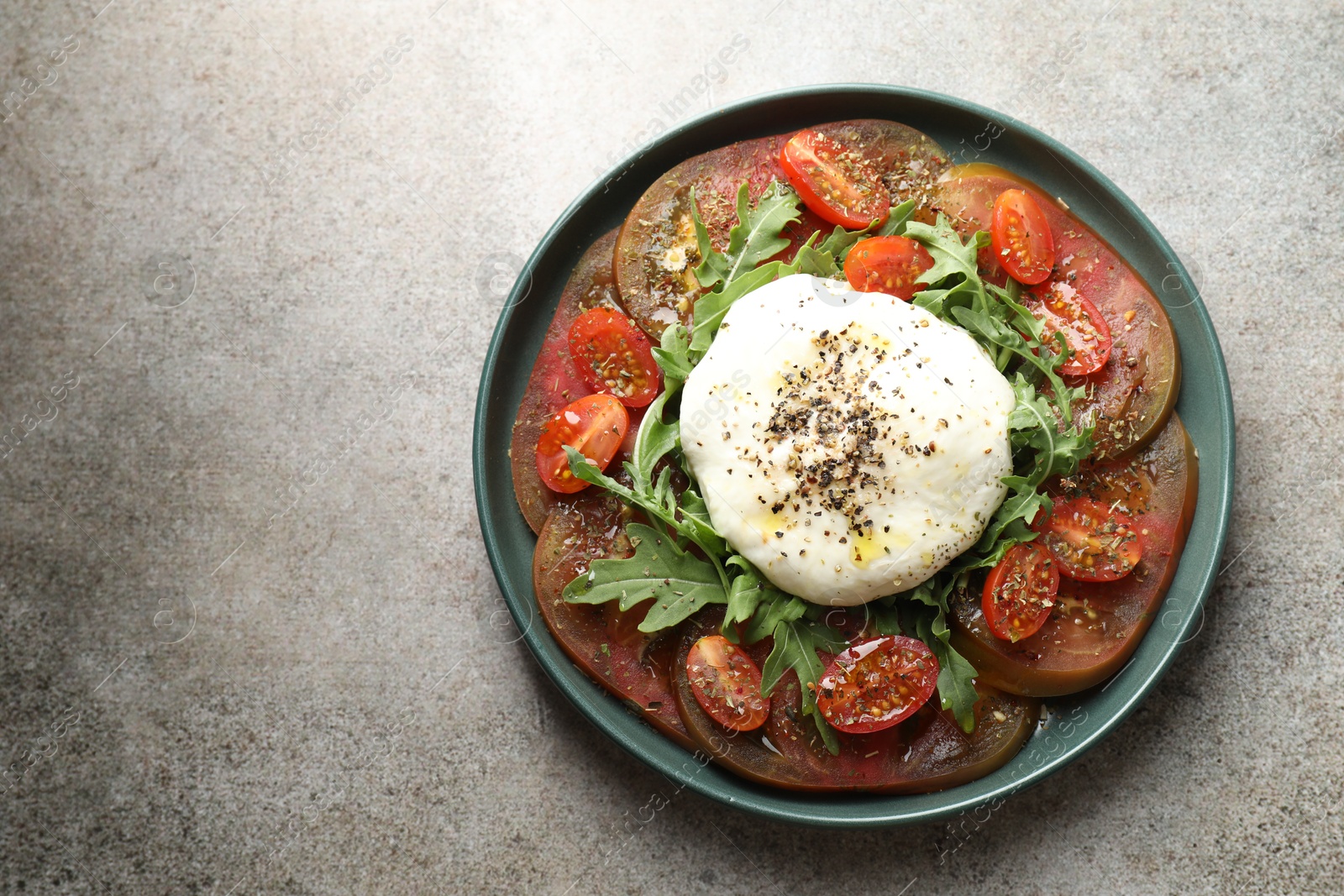 Photo of Delicious fresh burrata salad in bowl on gray textured table, top view. Space for text