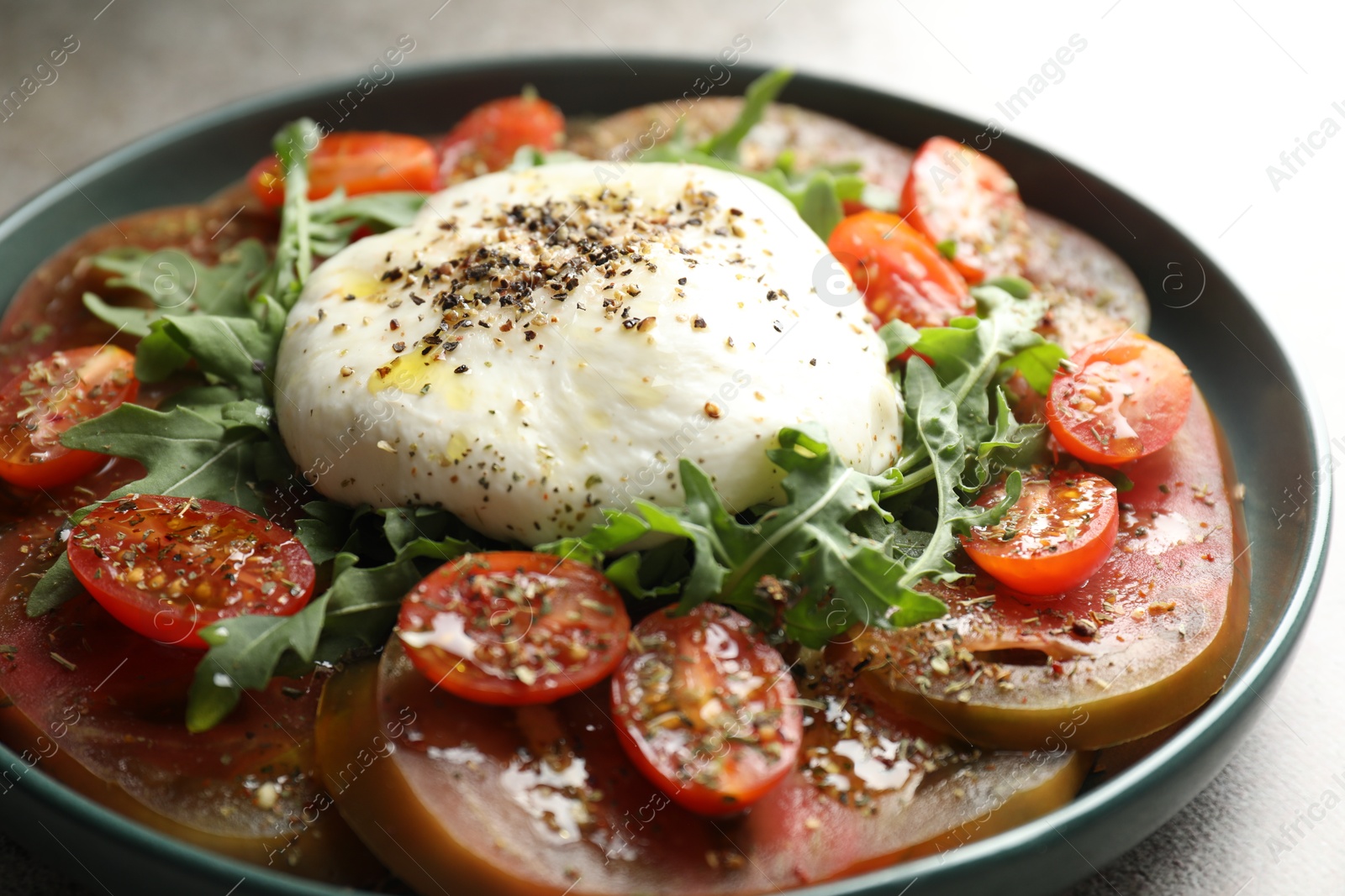 Photo of Delicious fresh burrata salad in bowl on gray table, closeup