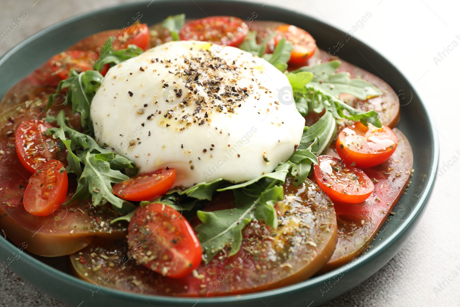 Photo of Delicious fresh burrata salad in bowl on gray textured table, closeup