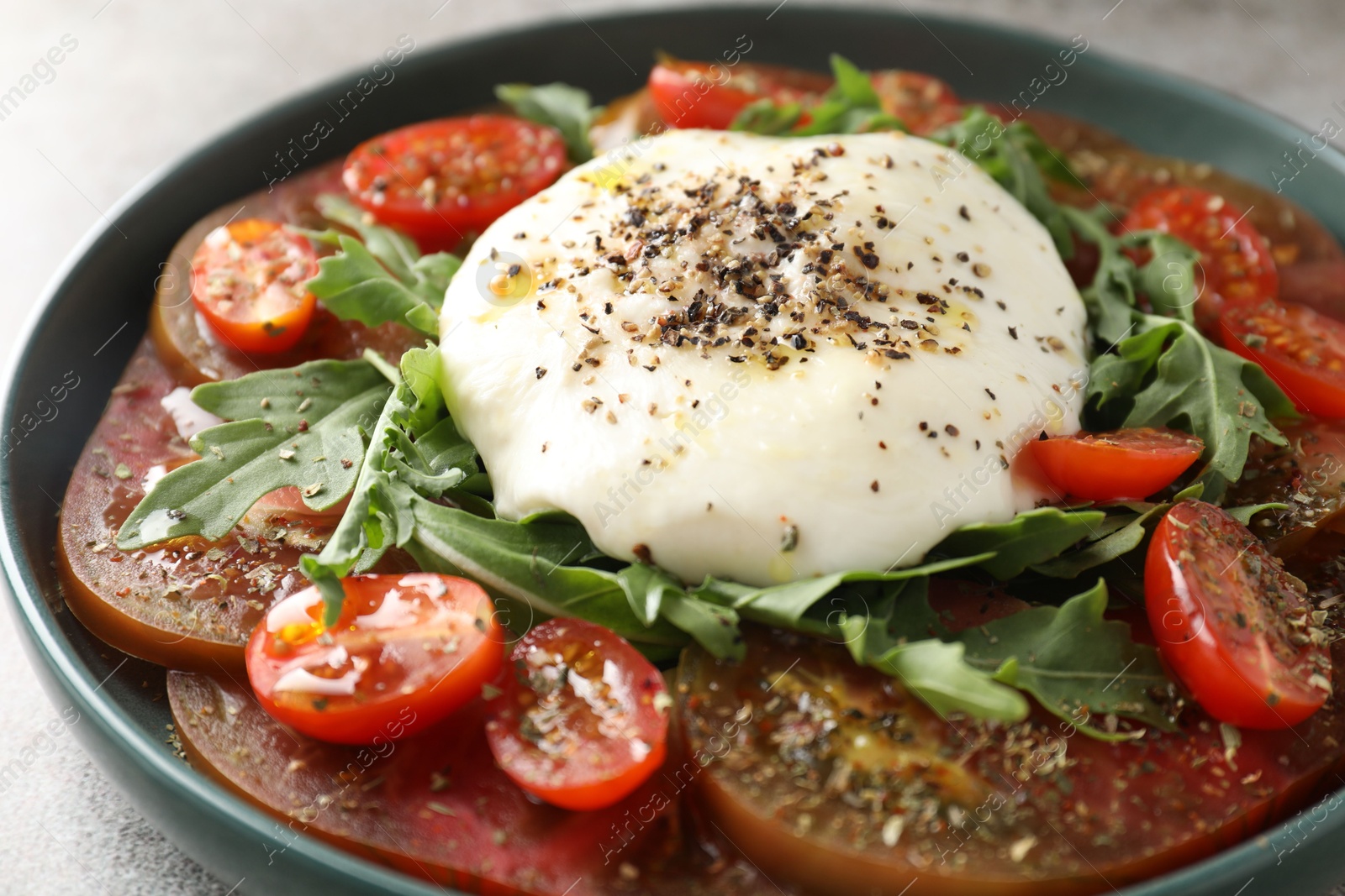 Photo of Delicious fresh burrata salad in bowl on gray table, closeup