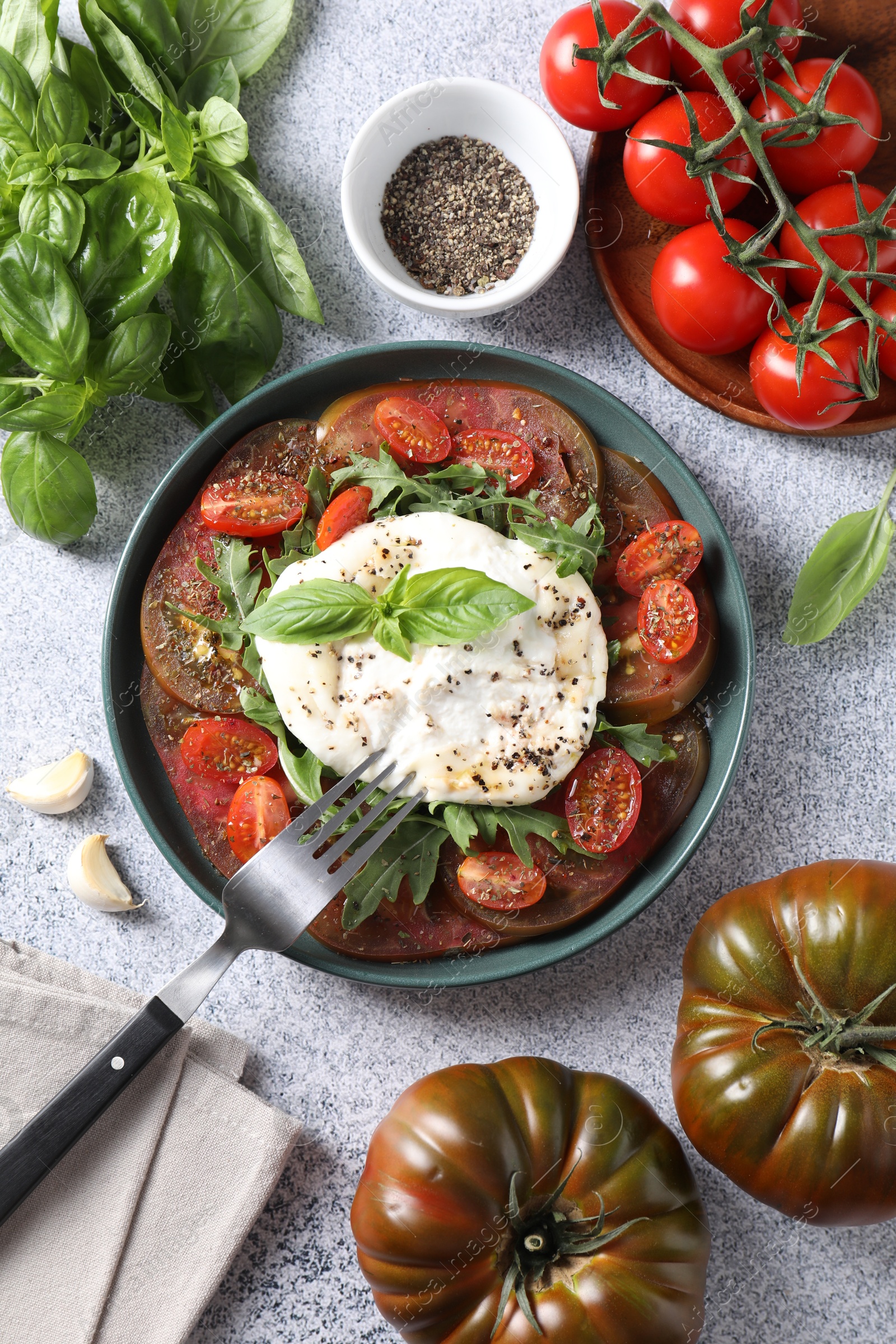 Photo of Delicious fresh burrata salad in bowl served on light gray textured table, flat lay