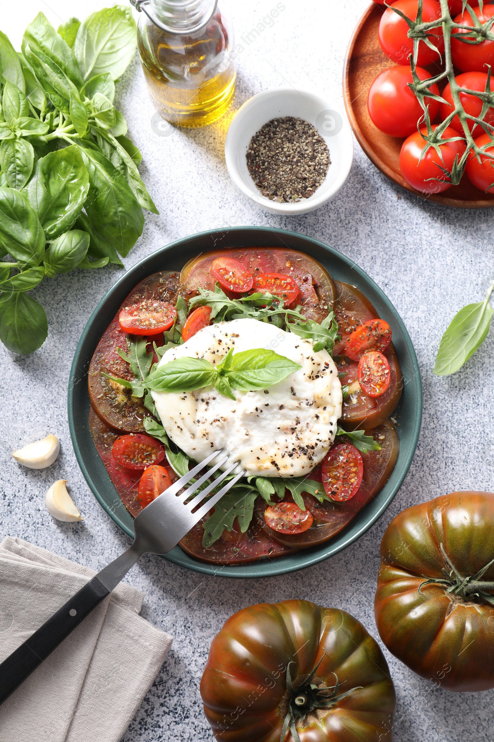 Photo of Delicious fresh burrata salad in bowl served on light gray textured table, flat lay