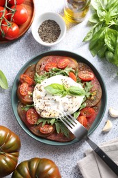 Delicious fresh burrata salad in bowl served on light gray textured table, flat lay