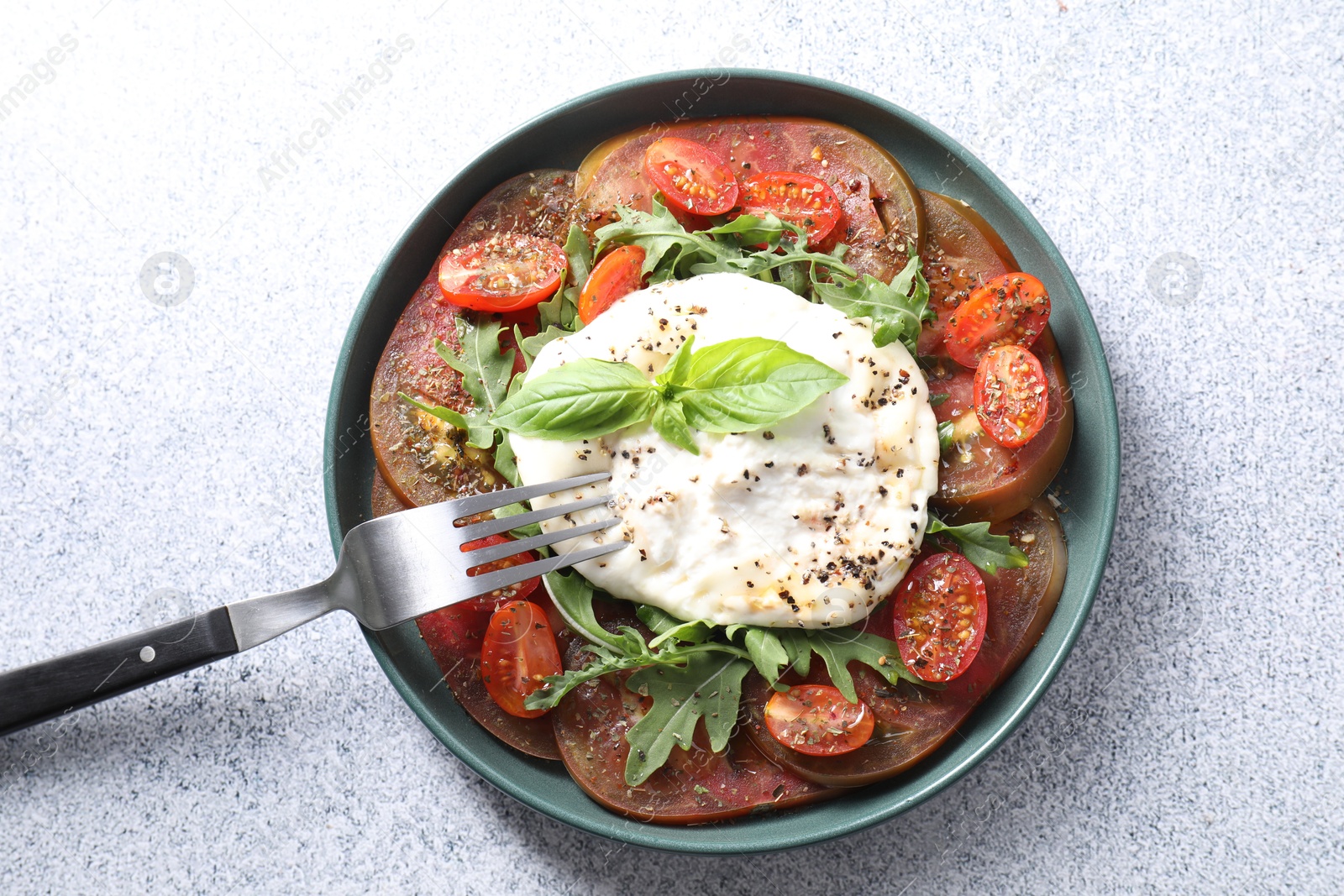 Photo of Delicious fresh burrata salad in bowl served on light gray textured table, top view