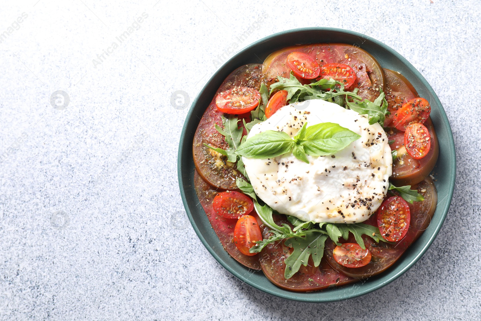 Photo of Delicious fresh burrata salad in bowl on light gray textured table, top view. Space for text