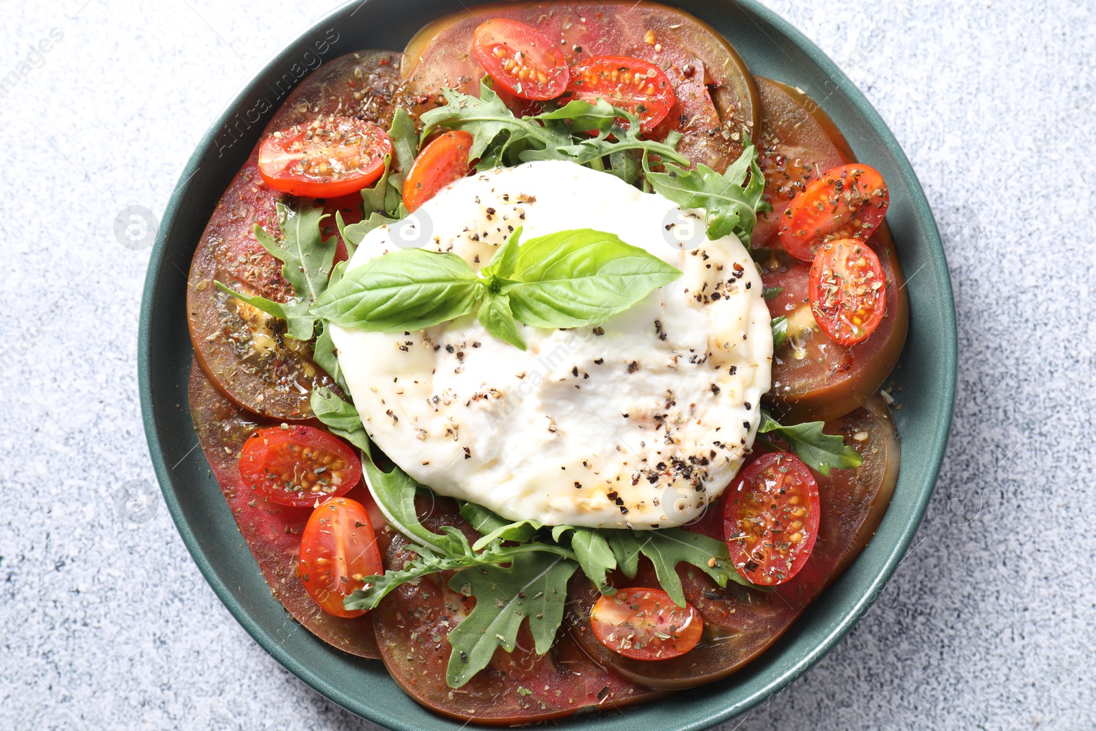 Photo of Delicious fresh burrata salad in bowl on light gray textured table, top view