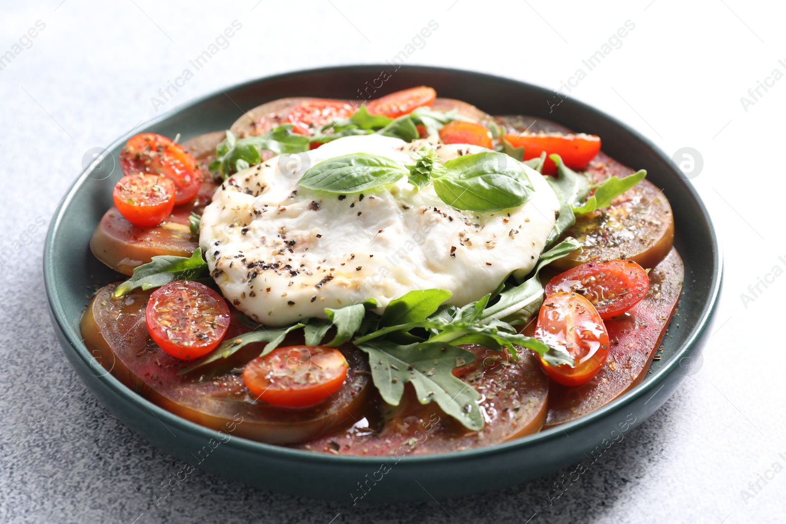 Photo of Delicious fresh burrata salad in bowl on light gray textured table, closeup