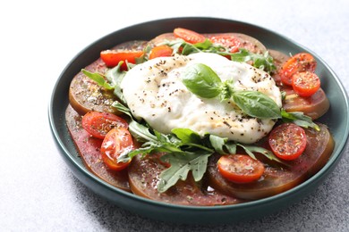 Photo of Delicious fresh burrata salad in bowl on light gray textured table, closeup