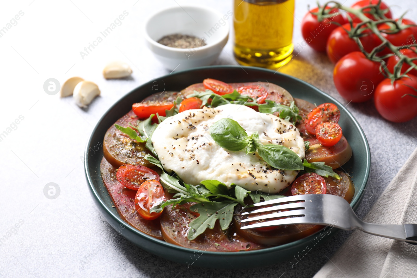 Photo of Delicious fresh burrata salad in bowl served on light gray textured table, closeup