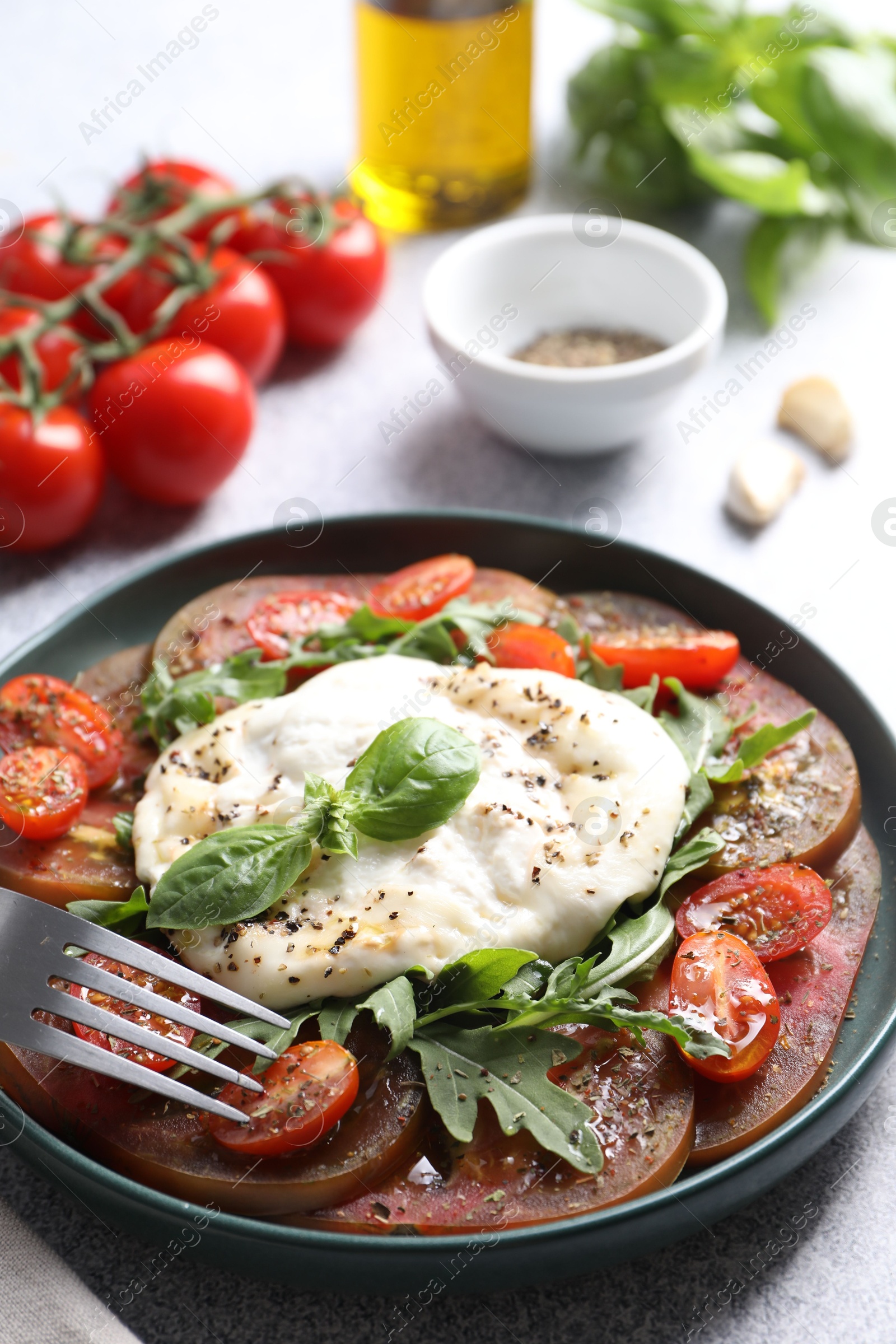 Photo of Delicious fresh burrata salad in bowl served on light gray table, closeup