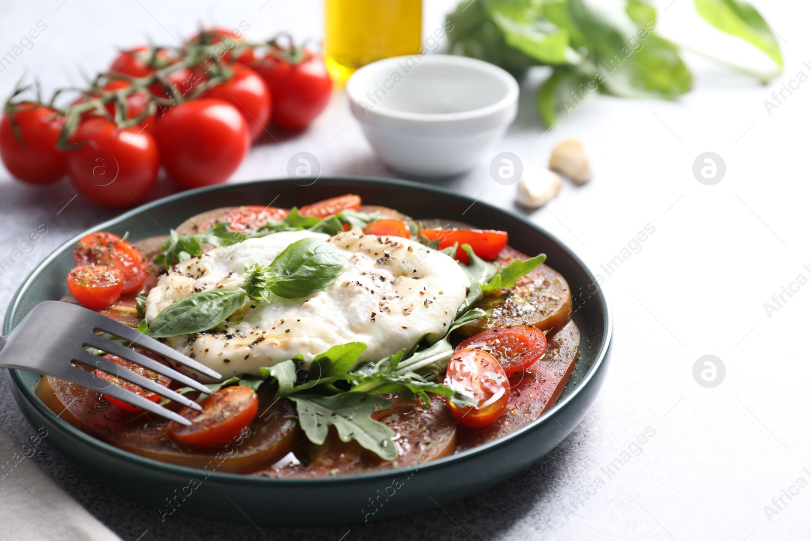 Photo of Delicious fresh burrata salad in bowl served on light gray textured table, closeup