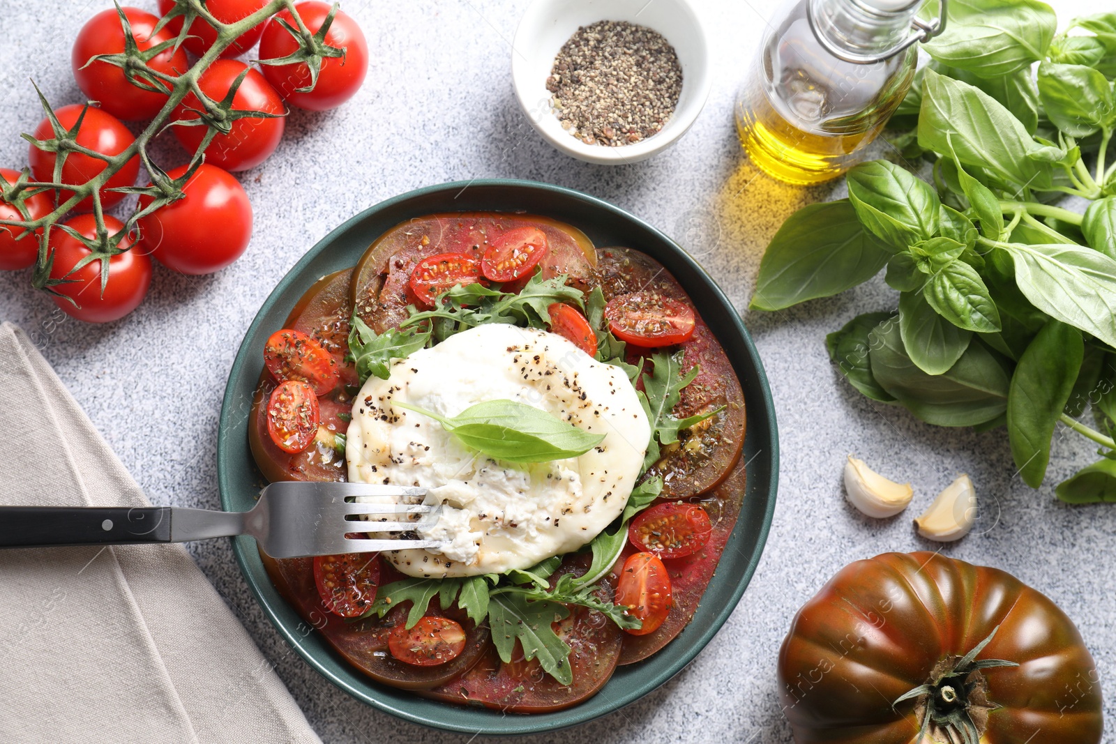 Photo of Delicious fresh burrata salad in bowl served on light gray textured table, flat lay