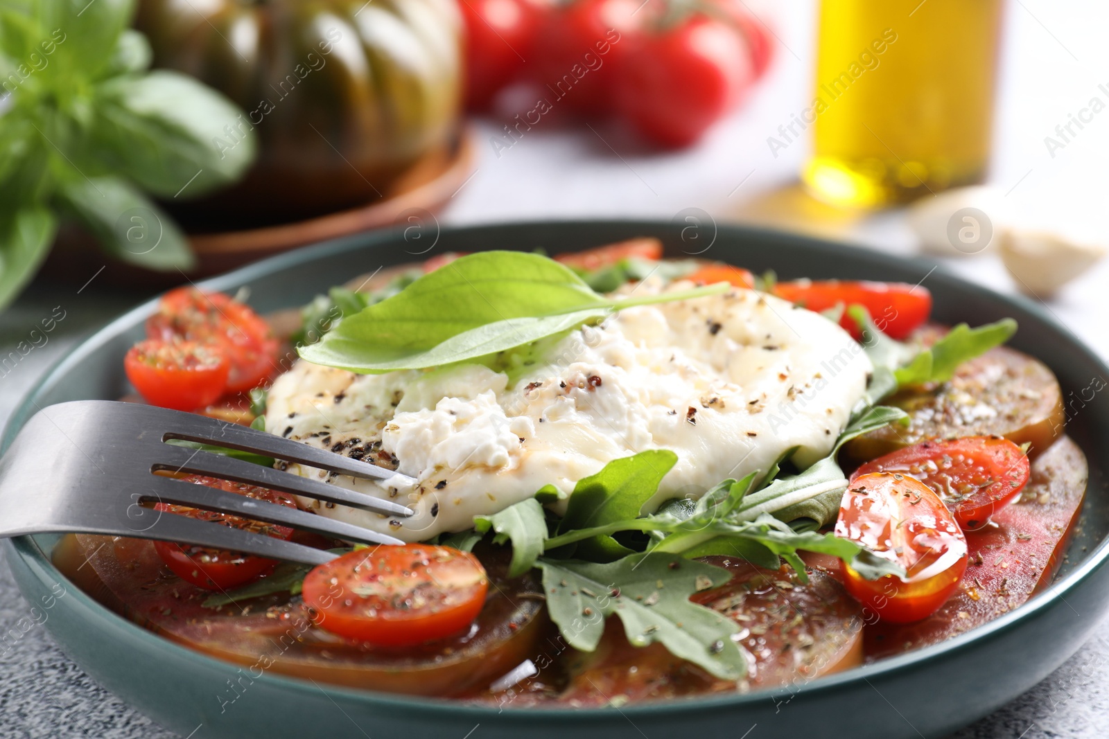 Photo of Delicious fresh burrata salad in bowl served on table, closeup