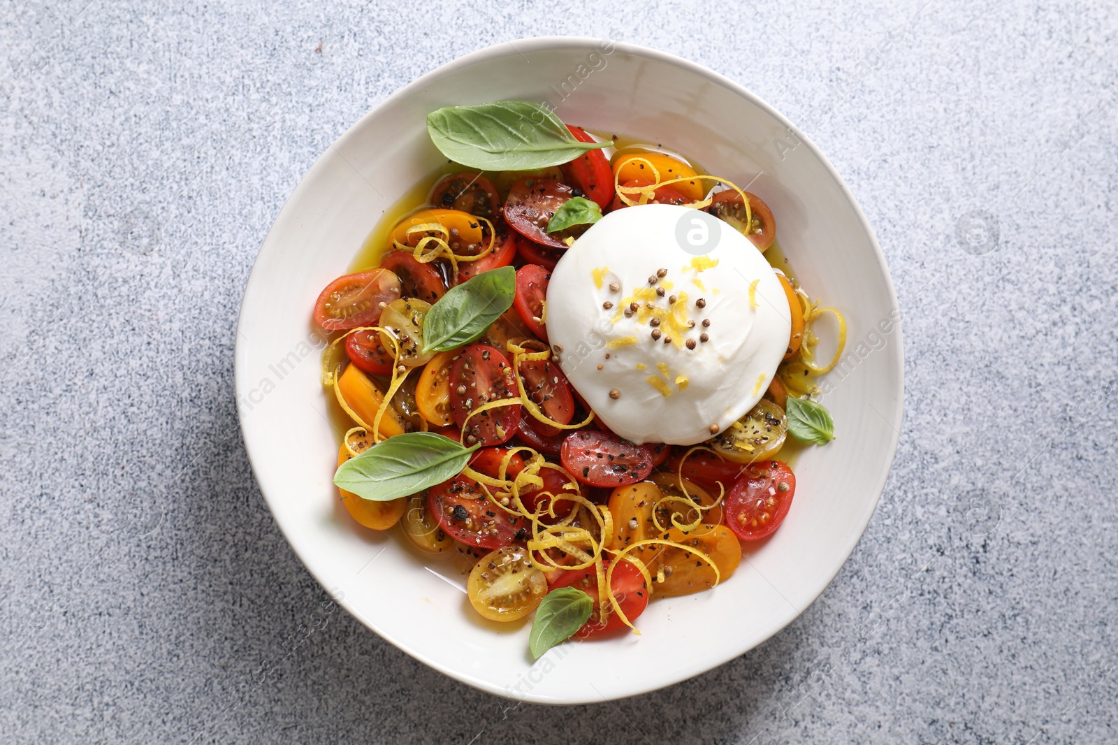 Photo of Delicious fresh burrata salad in bowl on light gray textured table, top view