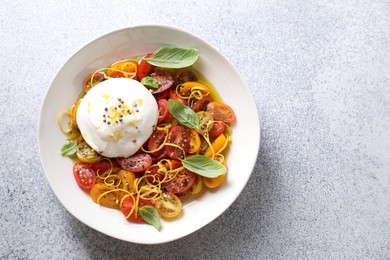 Delicious fresh burrata salad in bowl on light gray textured table, top view. Space for text