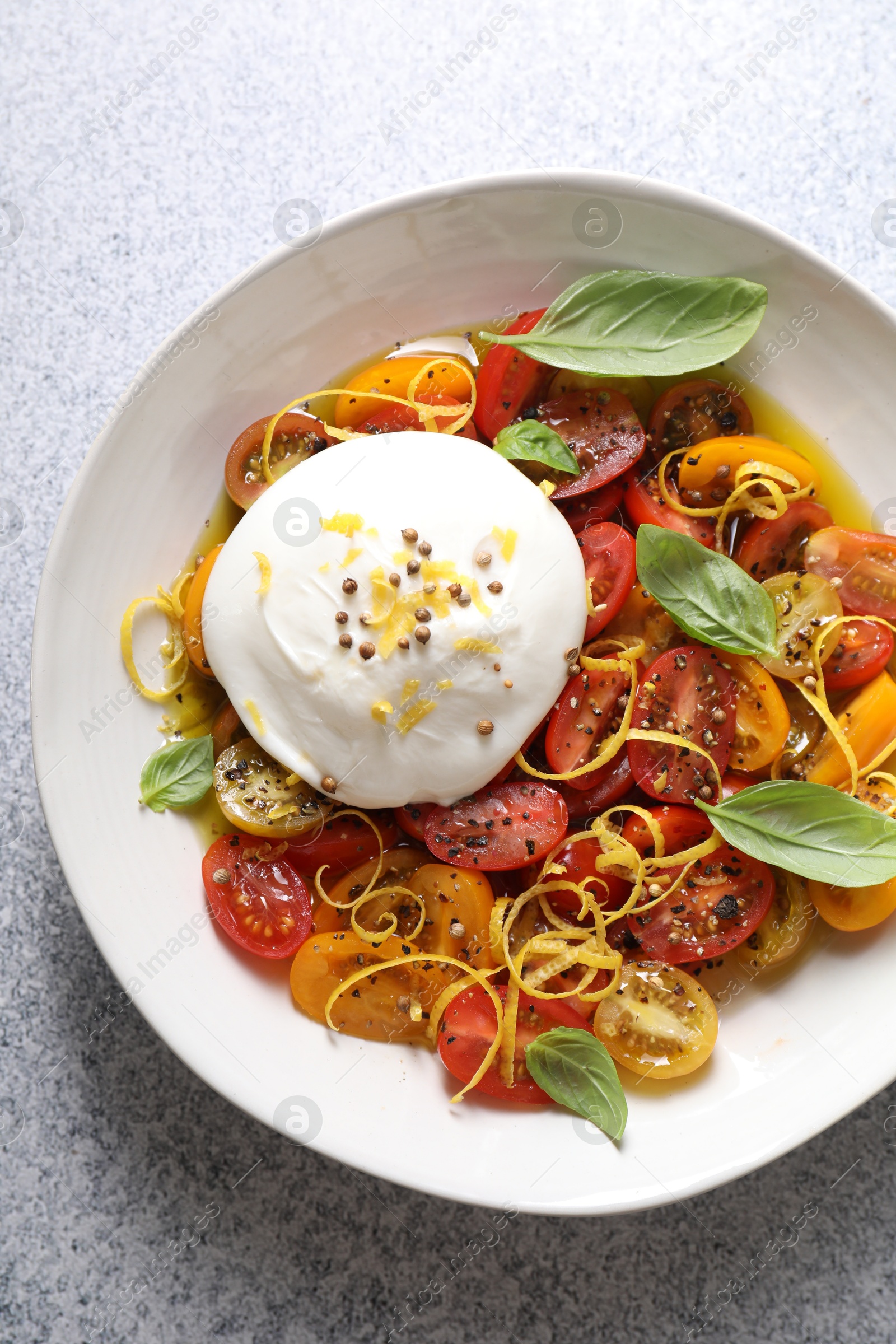 Photo of Delicious fresh burrata salad in bowl on light gray textured table, top view