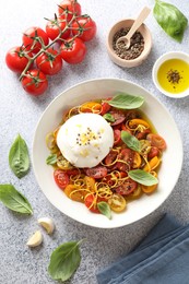 Photo of Delicious fresh burrata salad in bowl and ingredients on light gray textured table, flat lay