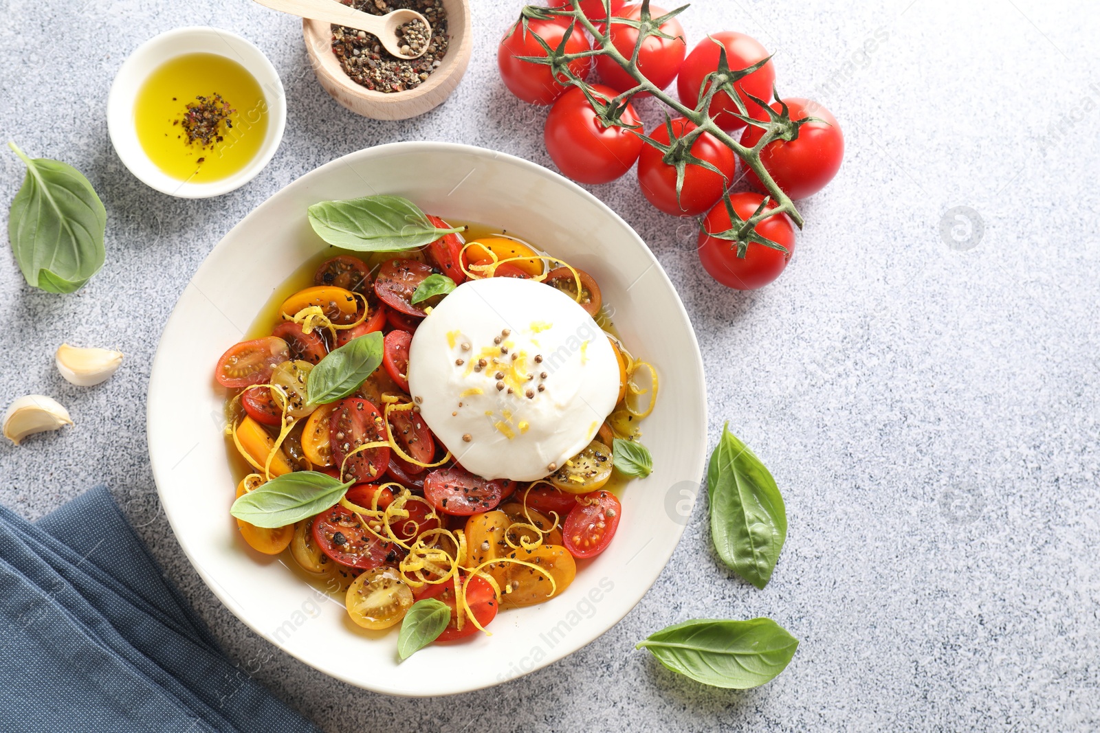 Photo of Delicious fresh burrata salad in bowl and ingredients on light gray textured table, flat lay