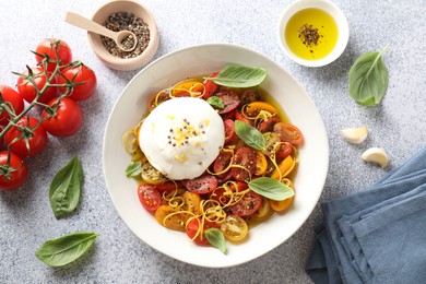 Photo of Delicious fresh burrata salad in bowl and ingredients on light gray textured table, flat lay