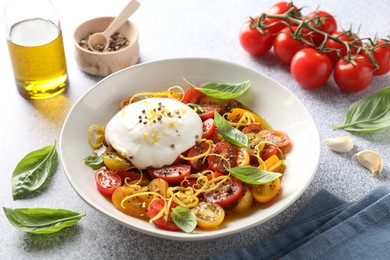 Delicious fresh burrata salad in bowl and ingredients on light gray textured table, closeup