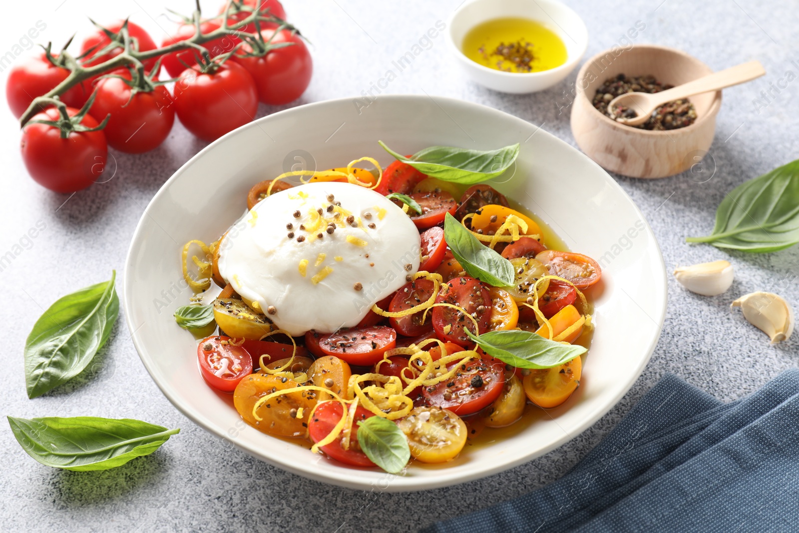 Photo of Delicious fresh burrata salad in bowl and ingredients on light gray textured table, closeup