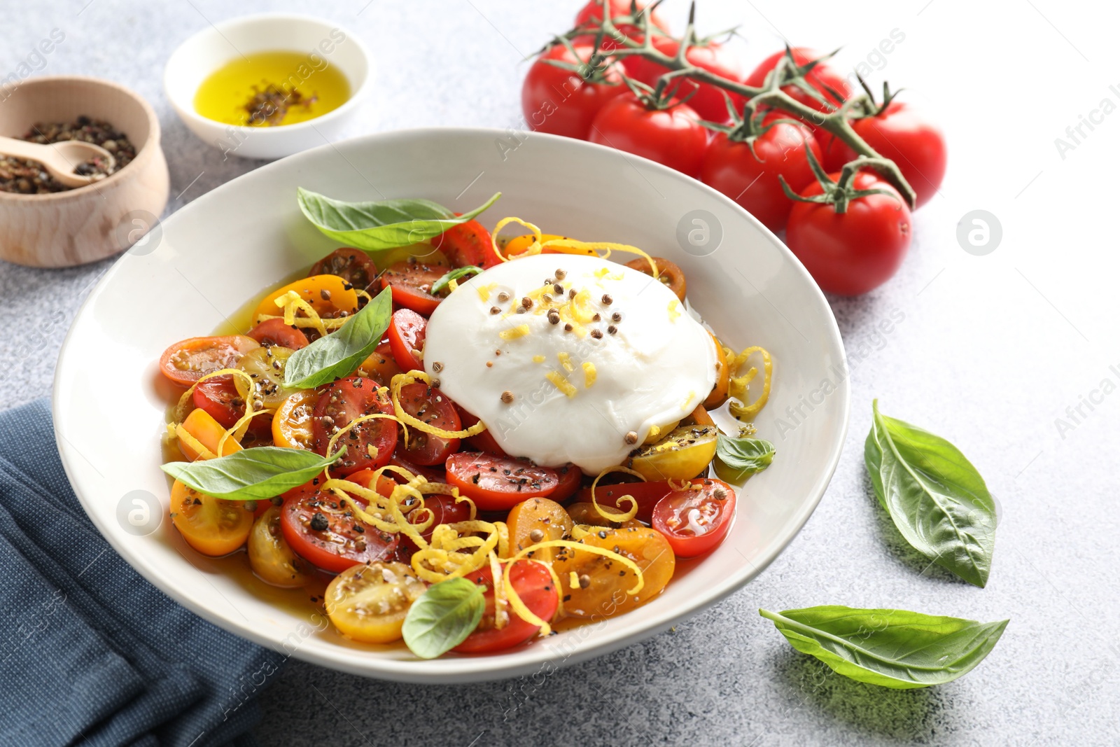 Photo of Delicious fresh burrata salad in bowl and ingredients on light gray textured table, closeup