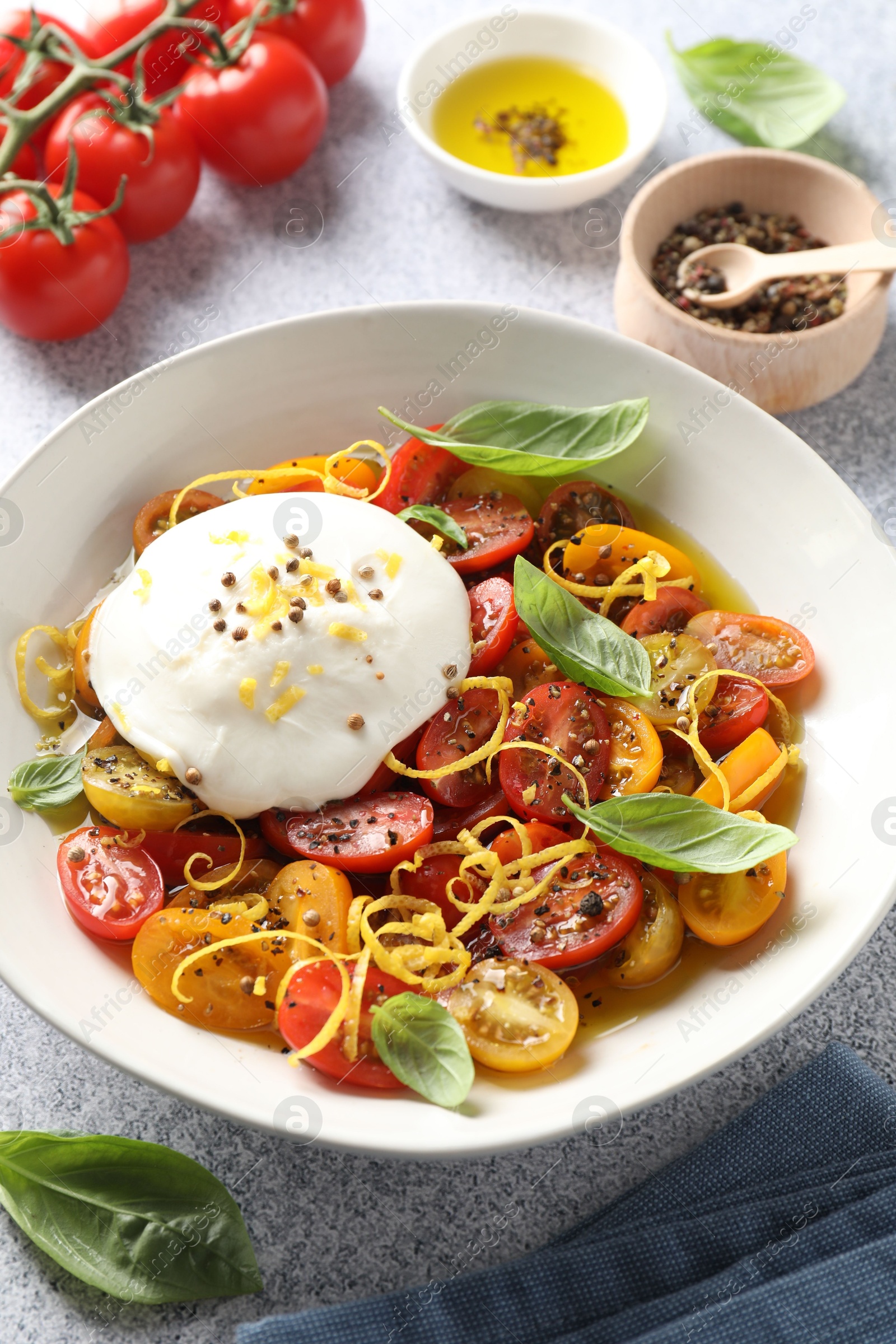 Photo of Delicious fresh burrata salad in bowl and ingredients on light gray textured table, closeup