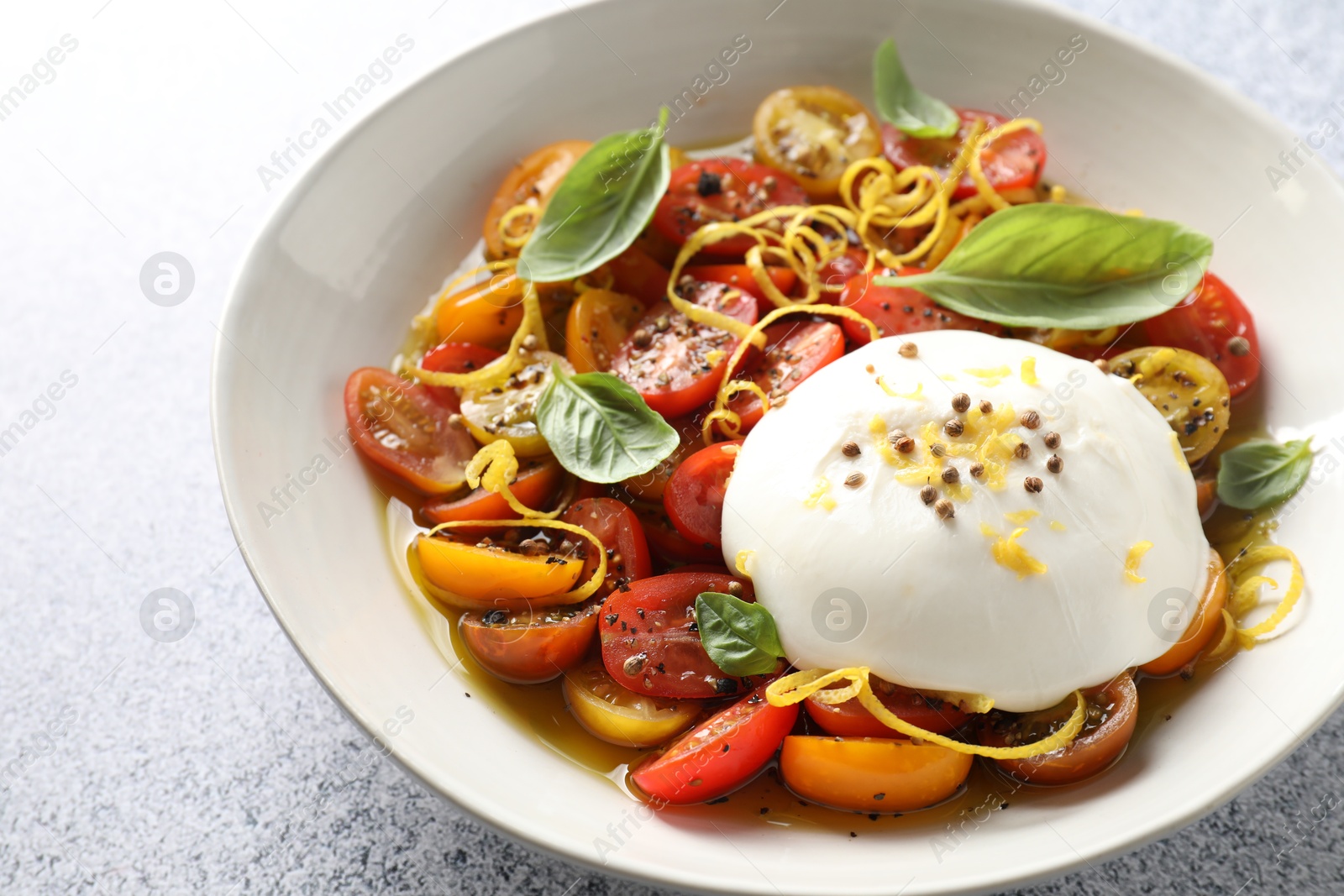 Photo of Delicious fresh burrata salad in bowl on light gray textured table, closeup