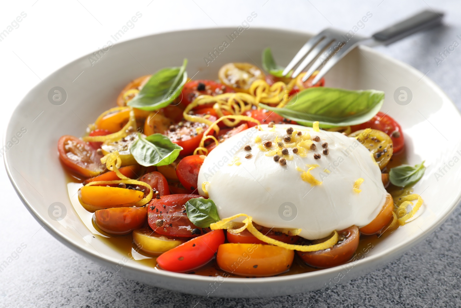 Photo of Delicious fresh burrata salad in bowl served on light gray table, closeup