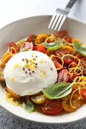 Photo of Delicious fresh burrata salad in bowl served on light gray table, closeup