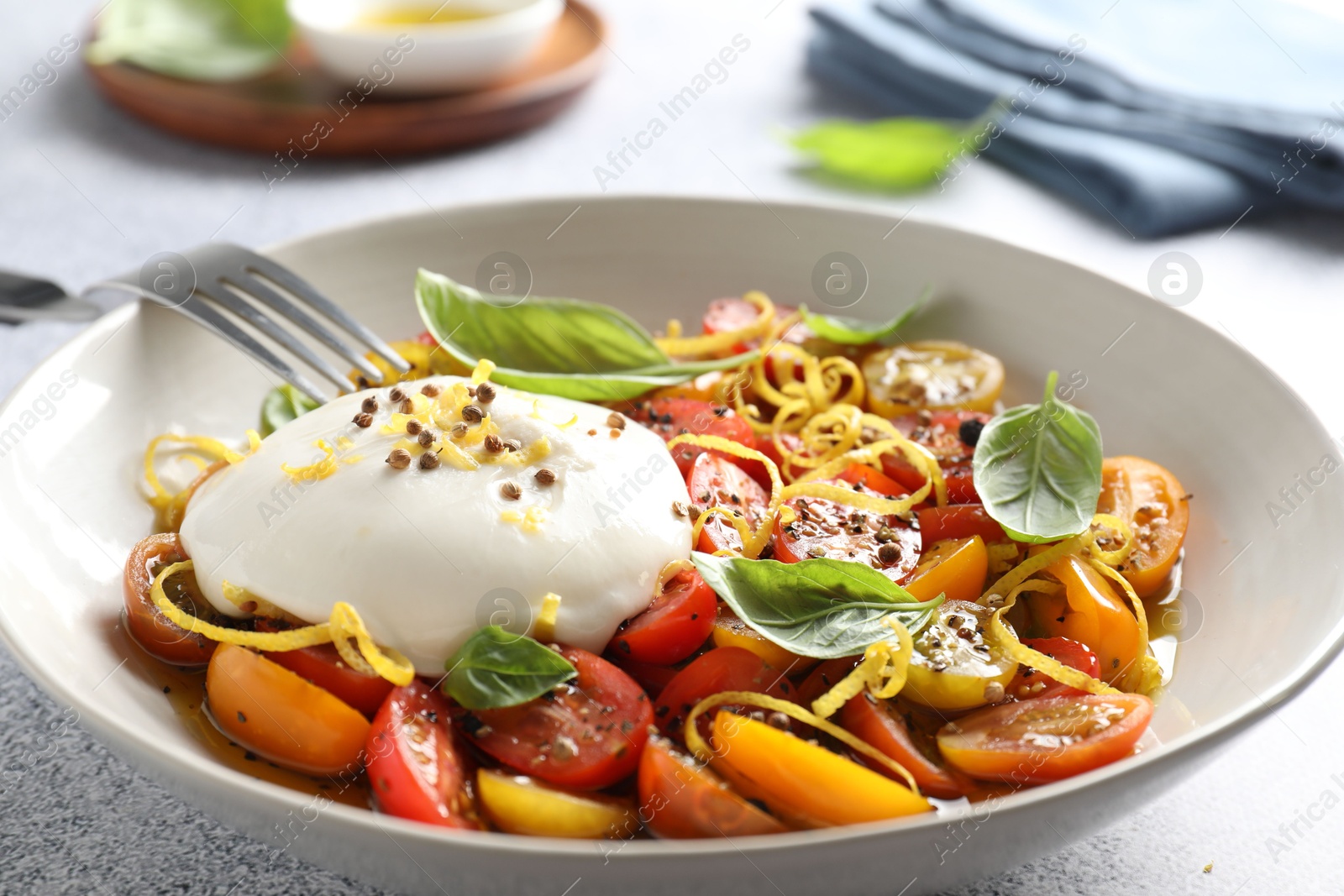 Photo of Delicious fresh burrata salad in bowl served on light gray textured table, closeup