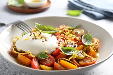 Delicious fresh burrata salad in bowl served on light gray textured table, closeup