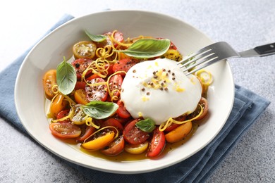 Photo of Delicious fresh burrata salad in bowl served on light gray textured table, closeup