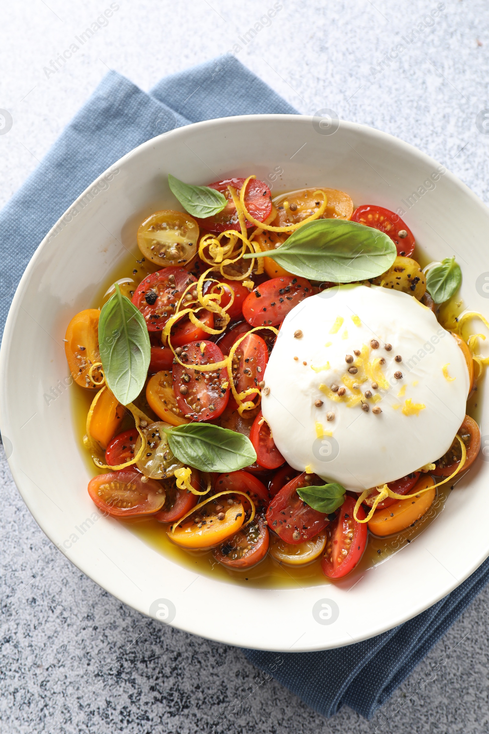 Photo of Delicious fresh burrata salad in bowl on light gray textured table, top view