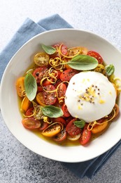 Delicious fresh burrata salad in bowl on light gray textured table, top view