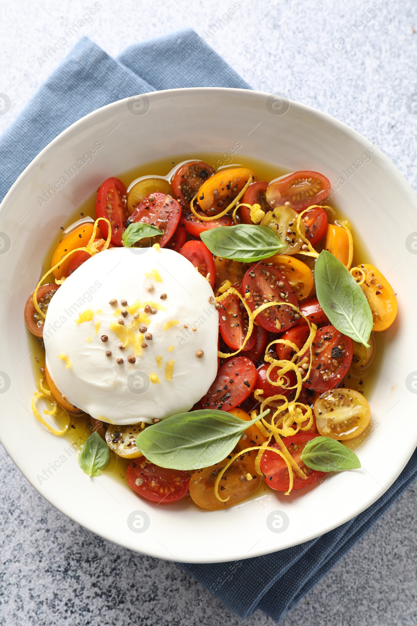 Photo of Delicious fresh burrata salad in bowl on light gray textured table, top view