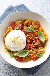 Photo of Delicious fresh burrata salad in bowl on light gray textured table, top view