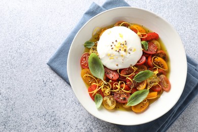 Photo of Delicious fresh burrata salad in bowl on light gray textured table, top view. Space for text