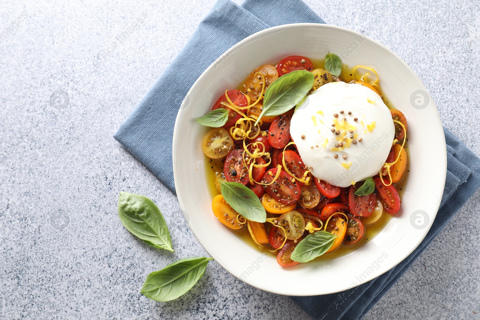 Photo of Delicious fresh burrata salad in bowl on light gray textured table, top view. Space for text