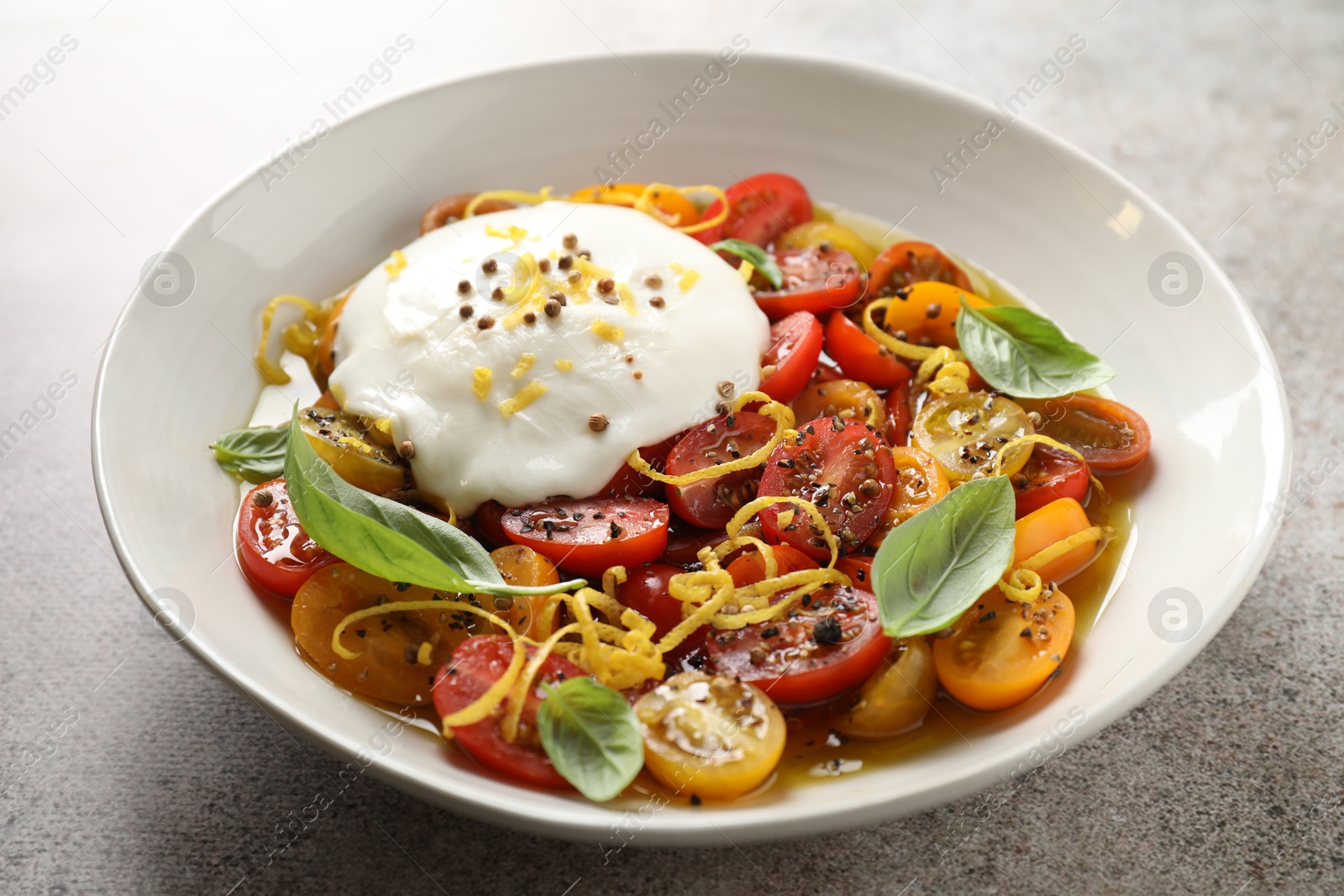 Photo of Delicious fresh burrata salad in bowl on gray textured table, closeup